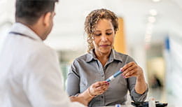 Woman looking at insulin pen while doctor looks at her 