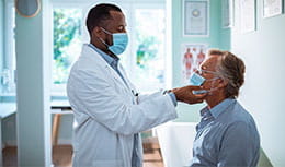 physician performing medical exam to elder patient sitting with mask on