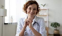 physician sitting on her chair leaning her elbows on a table, smiling contently