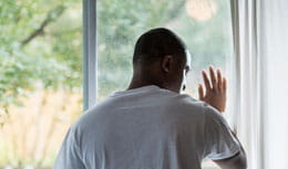 Upset young man looking outside window with hand against window