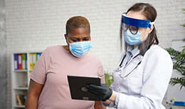 Doctor in protective shield mask talks to obese black woman