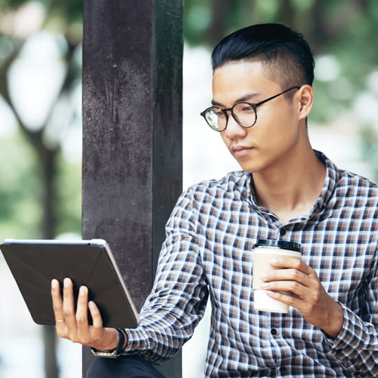 Young man outdoors looking at tablet with coffee