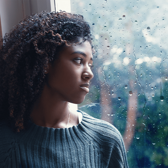 Upset young lady looking outside window on a rainy day