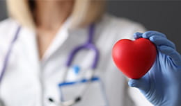 Doctor in rubber gloves holding red toy heart in his hands closeup