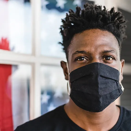 black man with a mask standing in front of a window with an american flag