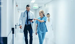 Female Surgeon and Doctor Walk Through Hospital Hallway
