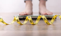 Female leg stepping on weigh scales with measuring tape