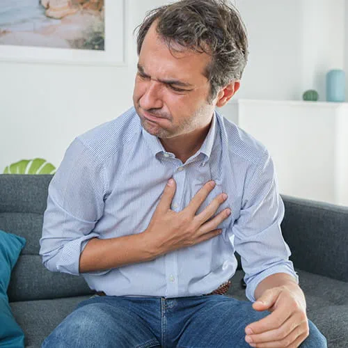 Man sitting on a couch clenching his chest
