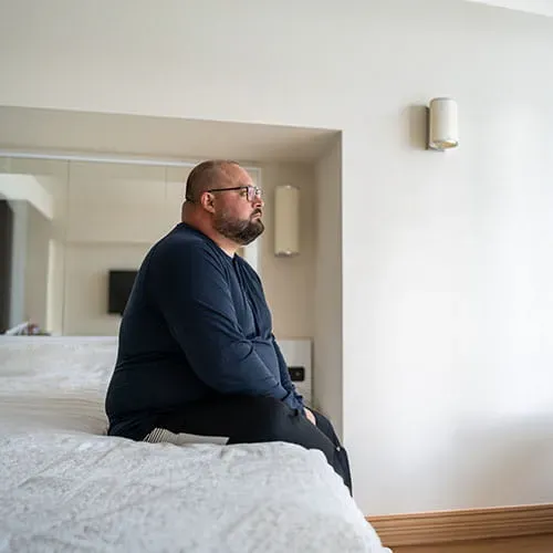 Obese man sitting on bed in hotel room