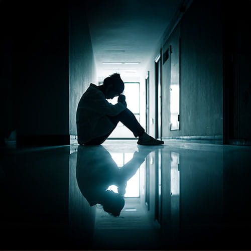 Silhouette of a woman with her head in her elbows in a dark hallway
