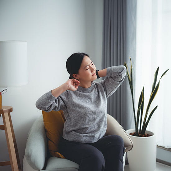 Woman suffering from neck pain sitting on armchair in living room at home