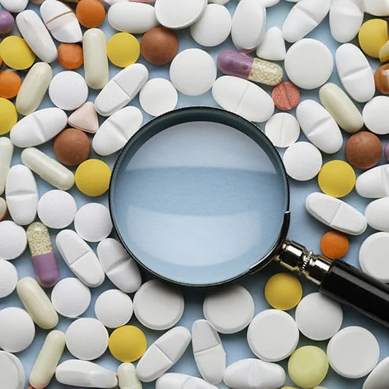 Magnifying glass surrounded by multicolored drugs.