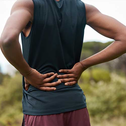 Fitness, nature and a person with back pain after hiking with a sports injury or accident. Tired, healthcare and an athlete or runner with muscle strain, inflammation or emergency after training