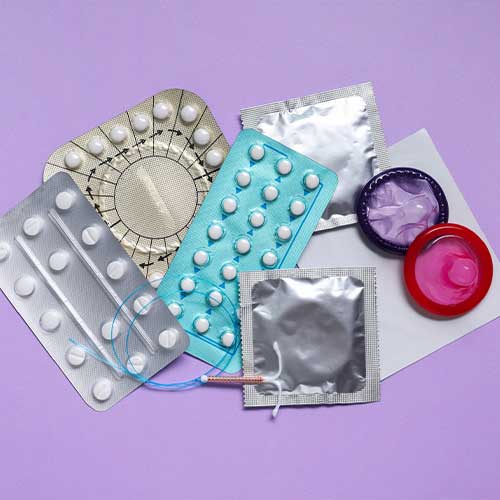 Contraceptive pills, condoms and intrauterine device on violet background, flat lay.