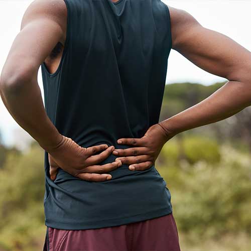 Fitness, nature and a person with back pain after hiking with a sports injury or accident. Tired, healthcare and an athlete or runner with muscle strain, inflammation or emergency after training
