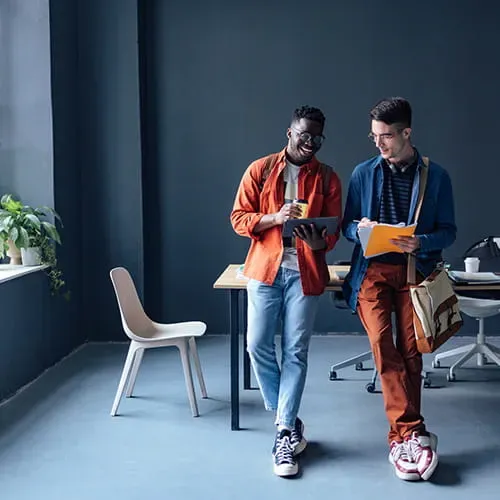 Two male students leaning on a table while looking at a tablet.