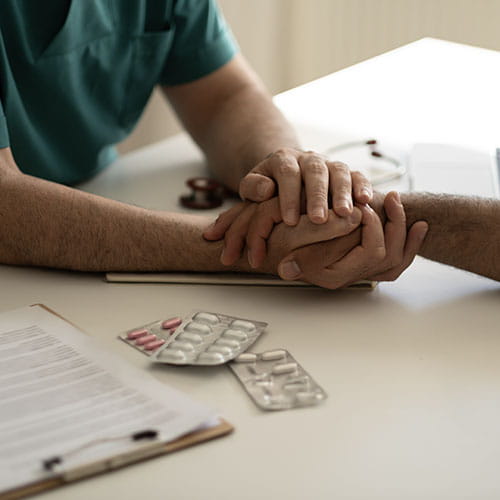 Clinician holding a patient's hand with pills on the table
