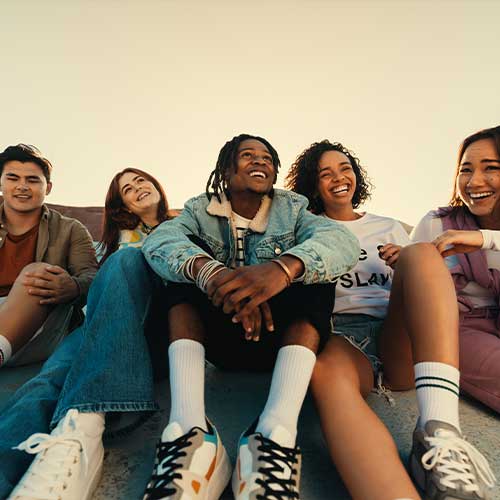 Happy group of friends sitting together outdoors, smiling and laughing, enjoying their time in a sunny setting.