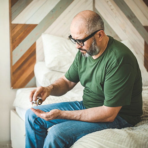 Man sitting on a bed taking pills
