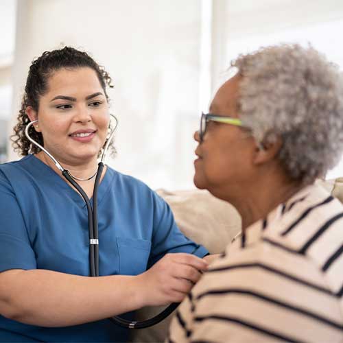 Nurse listening to senior patient's heartbeat during home visit