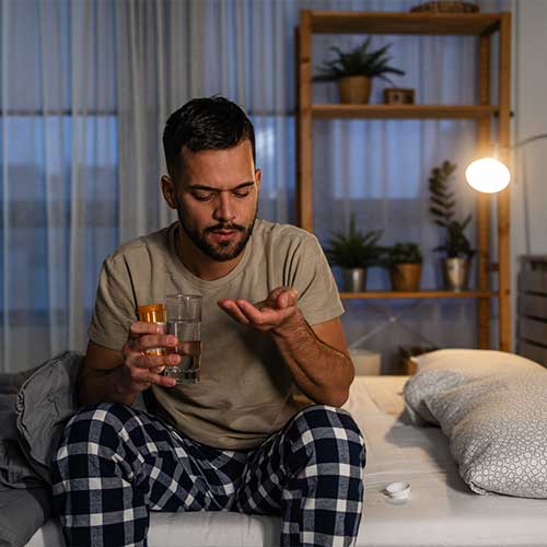 Portrait of a young man holding medicaments in one hand and a glass of water in the other. He is about to drink a recommended dose.