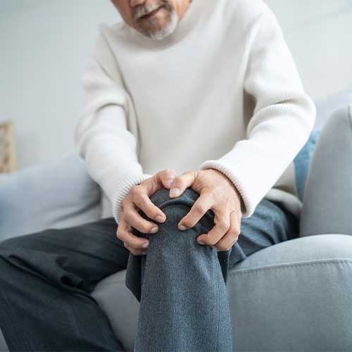 Asian Senior elderly disabled man sit on sofa suffer from injured leg. Mature older male patient sitting on couch in living room has knee problem and feel painful. Insurance and Healthcare concept.