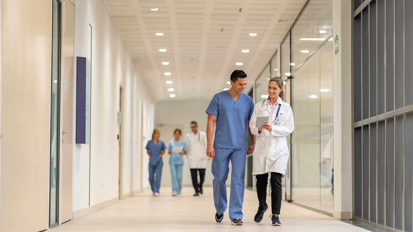Medical works walking down a hospital corridor while looking at a tablet
