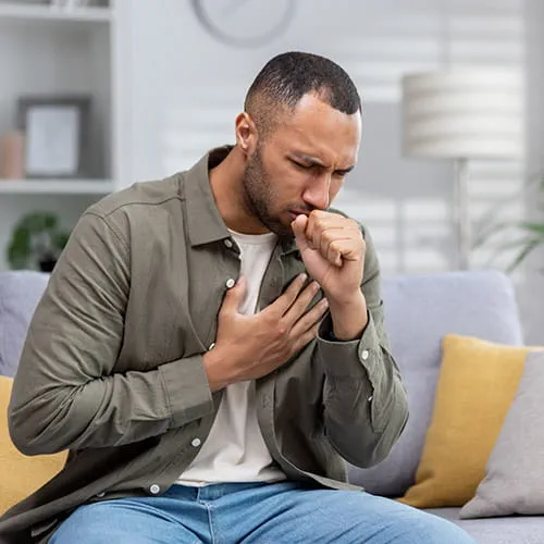Man sitting on a couch coughing