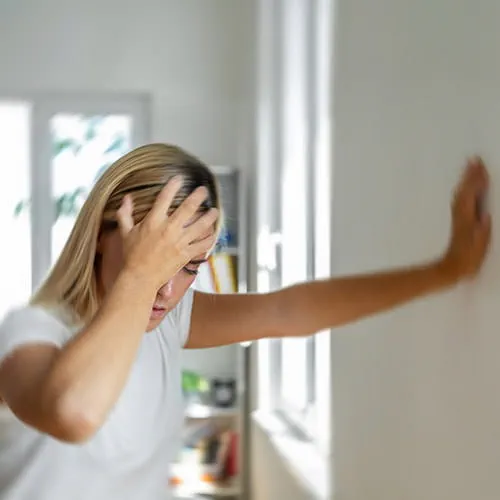 Woman leaning against a wall with her hand on her head