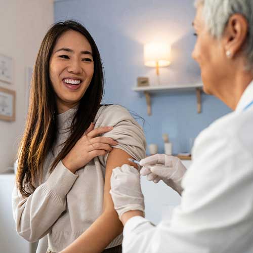Senior Caucasian female doctor, giving an flu vaccine to a female patient Japanese ethnicity, during an annual medical check-up