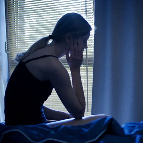Woman sitting on a bed resting her hand on her face
