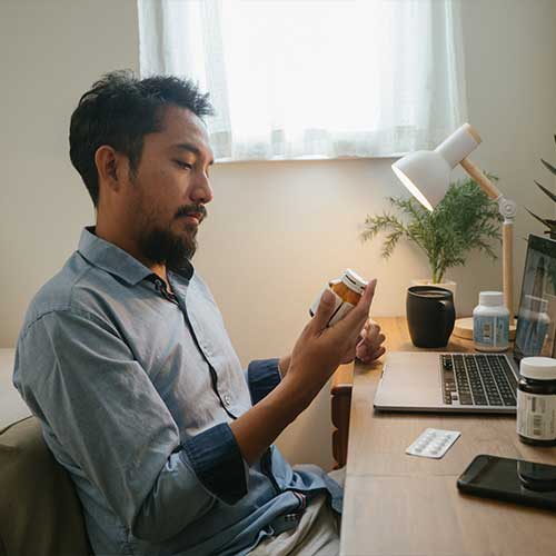 Asian man looking at pill bottle and listening to women doctor in consultation medicine to video conference at home.