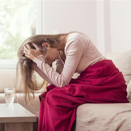 Woman sitting on a couch bent over with her hands on her head