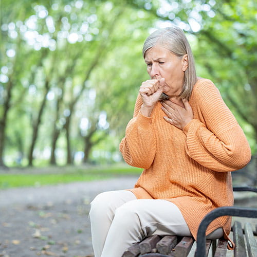 Woman coughing outside on a bench