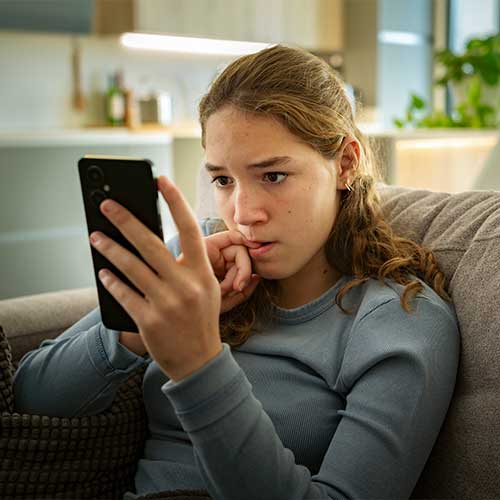 Portrait of a nervous teen girl looking at her smartphone biting her nails worried about bad news