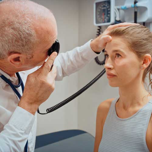 Doctor or optometrist check eye of a woman patient while consulting in a medical clinic. Healthcare expert or professional doing a test or exam on eyes vision in a hospital workplace through a lens
