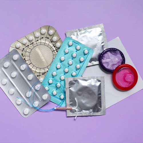 Contraceptive pills, condoms and intrauterine device on violet background, flat lay. Different birth control methods