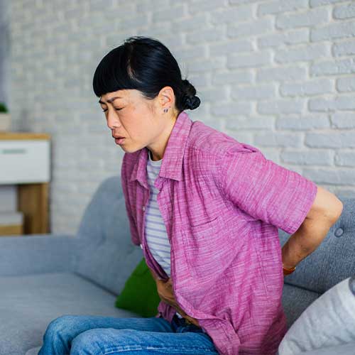 Woman Experiencing Lower Back Pain While Sitting on Sofa