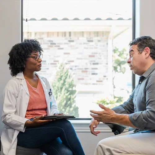 The serious mid adult female doctor listens to the mature adult male patient as he gestures and speaks.