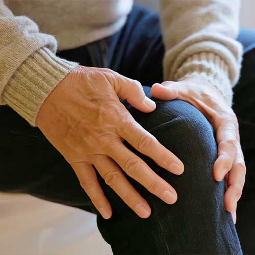 Closeup asian elderly male suffer from knee pain - he sits on sofa feels so painful in bedroom at home