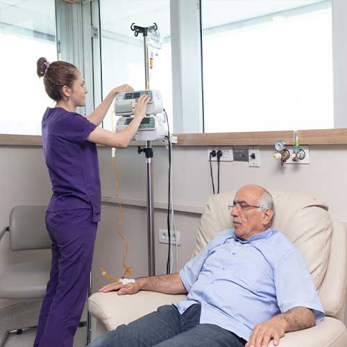 Nurse getting ready to take a patient to a medical procedure. A female nurse takes care of a male patient in the IV room. She's making preparations to give him medicine. Room equipped with health equipment.