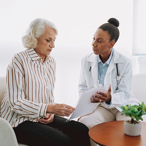 Doctor in a white coat reviewing a document with an older woman.