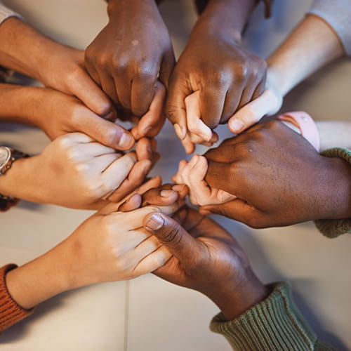 A group of people with different skintones holding hands in a circle.