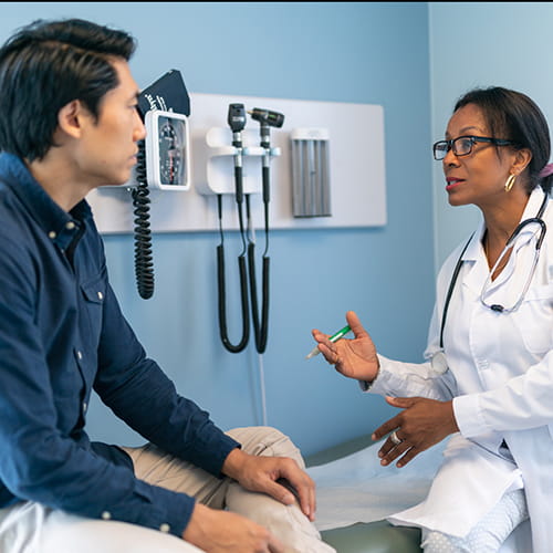 Doctor talking with a male patient seated on an exam table.