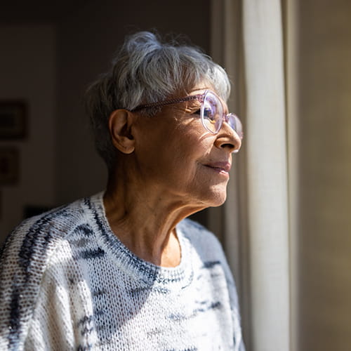 A elderly woman gazes out a window.