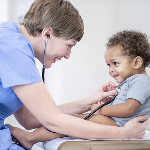 A doctor uses a stethoscope to check the heart of a smiling baby.