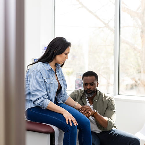 Adult couple hold hands in an examination room.
