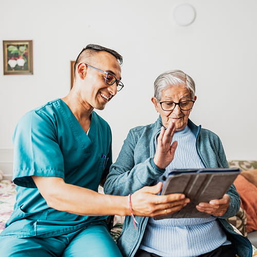 Caregiver helping senior woman use digital tablet at home.