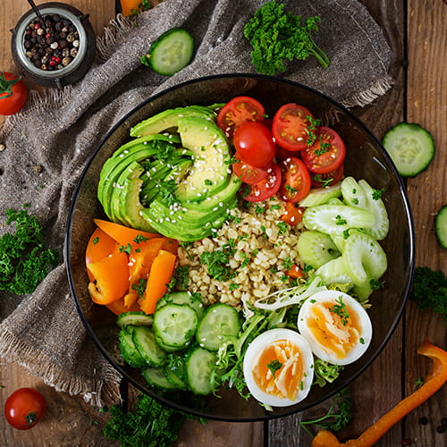 Plate filled with bulgur porridge, eggs, avocado, tomatoes, cucumber, celery and bell peppers.