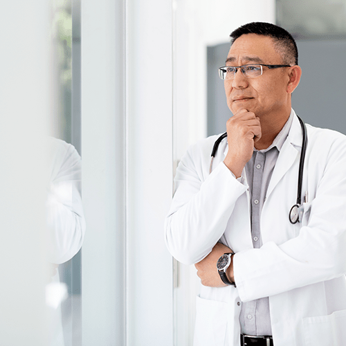 A concerned doctor thoughtfully looks out a window.